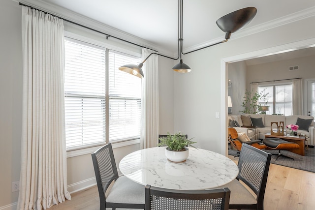 dining room with ornamental molding, light wood-style flooring, visible vents, and baseboards