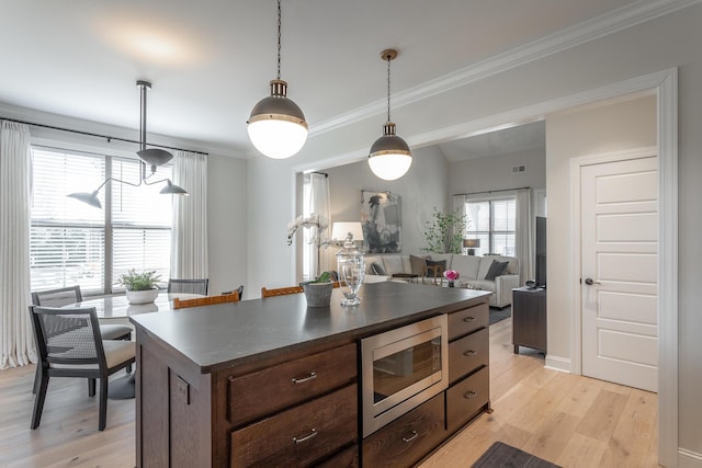 kitchen with hanging light fixtures, ornamental molding, light wood-type flooring, stainless steel microwave, and dark countertops