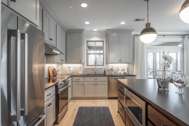 kitchen with stainless steel appliances, dark countertops, tasteful backsplash, a sink, and under cabinet range hood