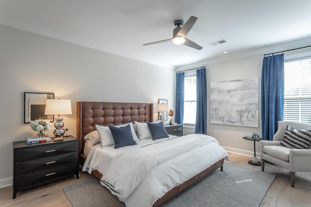 bedroom featuring light wood-style flooring, a ceiling fan, visible vents, baseboards, and ornamental molding