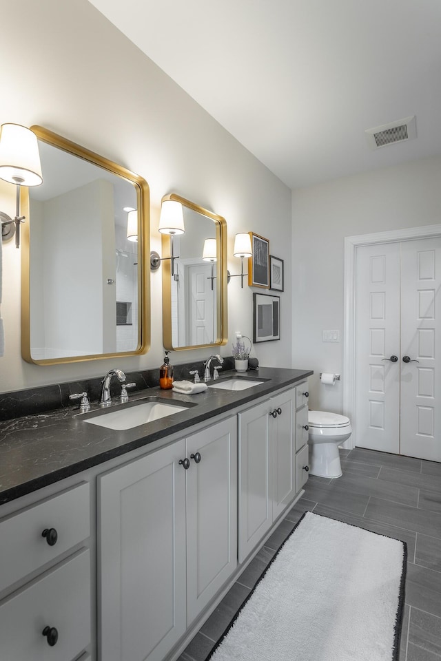 bathroom with toilet, double vanity, a sink, and visible vents