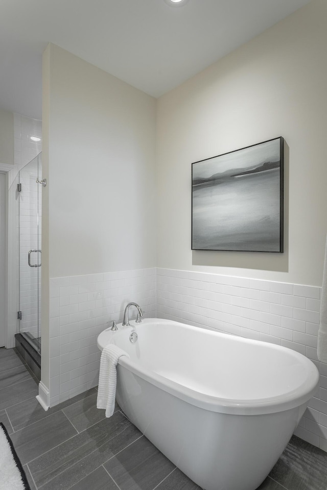 bathroom featuring a freestanding tub, a shower stall, tile walls, and wainscoting