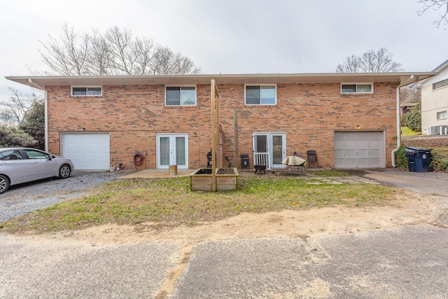 view of front of house featuring driveway, french doors, an attached garage, and brick siding