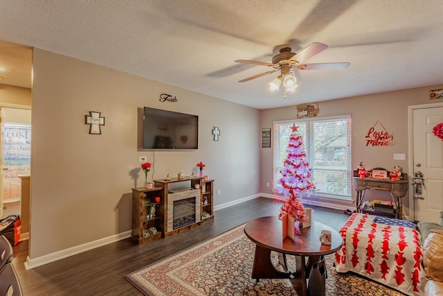 living area featuring ceiling fan, dark wood-style flooring, a glass covered fireplace, and baseboards