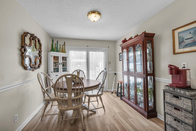 dining area with a textured ceiling, light wood-type flooring, and baseboards