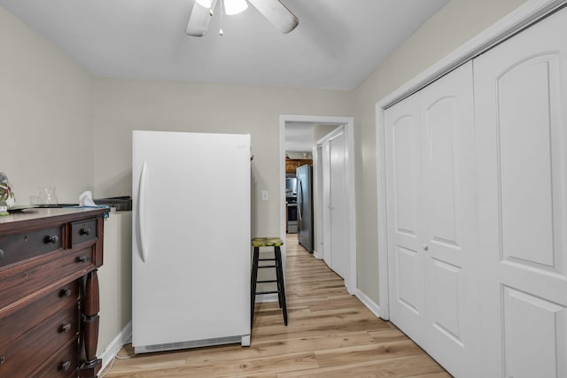 interior space with light wood-type flooring, freestanding refrigerator, baseboards, and a ceiling fan