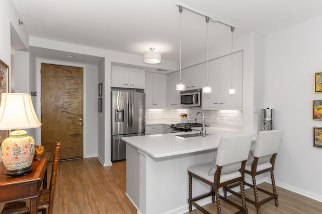 kitchen with a breakfast bar, a peninsula, a sink, appliances with stainless steel finishes, and tasteful backsplash