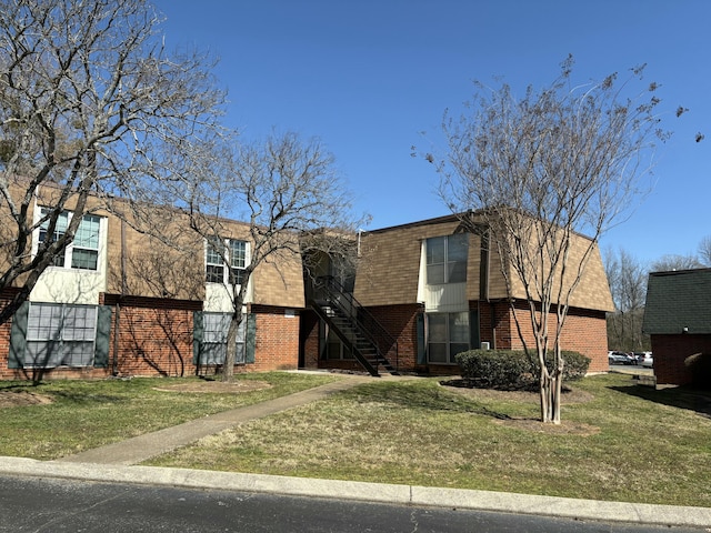 view of front facade featuring brick siding, a front lawn, and stairway