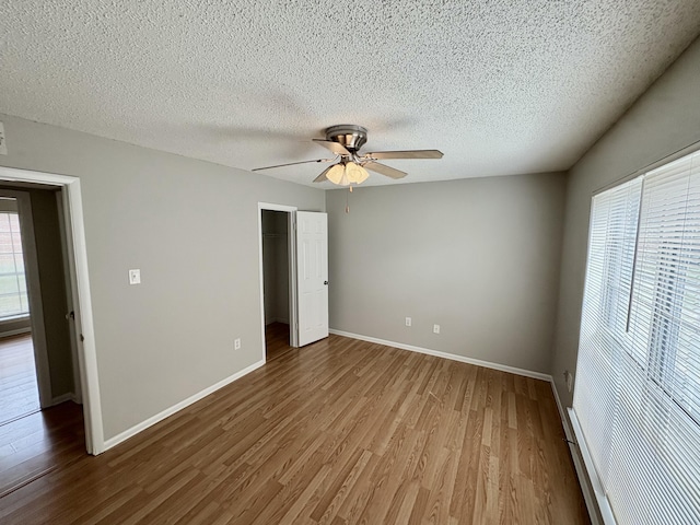 unfurnished bedroom with a closet, ceiling fan, a textured ceiling, wood finished floors, and baseboards