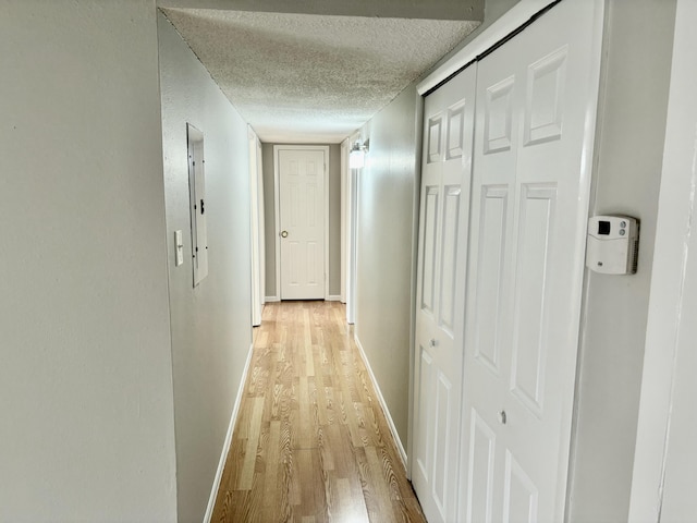 hallway featuring light wood-type flooring, a textured ceiling, and baseboards