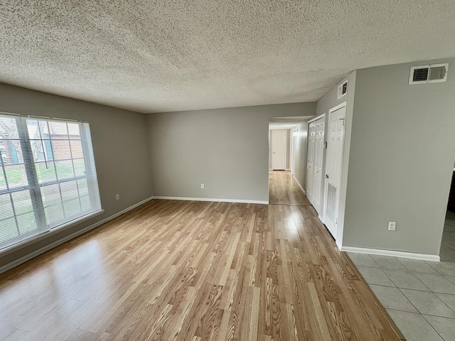 spare room with a textured ceiling, wood finished floors, visible vents, and baseboards