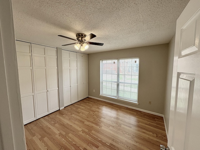 unfurnished bedroom featuring baseboards, multiple closets, a ceiling fan, and light wood-style floors