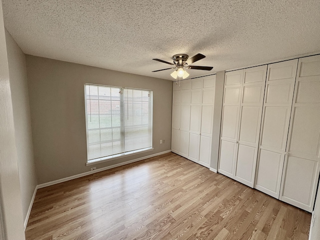 unfurnished bedroom with a textured ceiling, light wood-style flooring, a ceiling fan, multiple closets, and baseboards