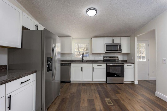 kitchen with appliances with stainless steel finishes, dark countertops, white cabinetry, and a sink