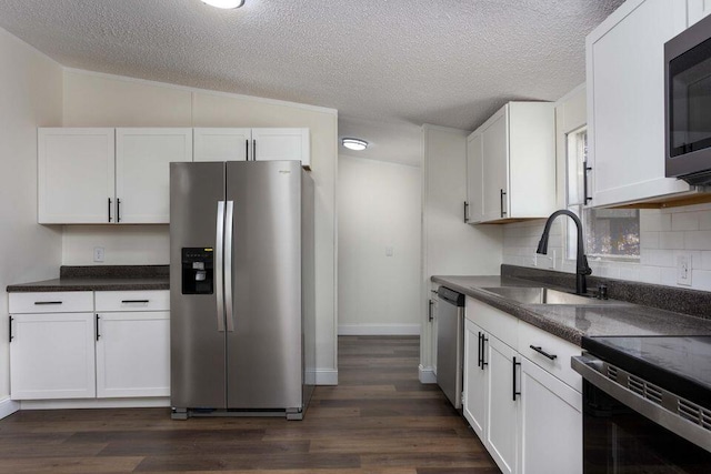 kitchen featuring dark countertops, appliances with stainless steel finishes, white cabinets, and a sink