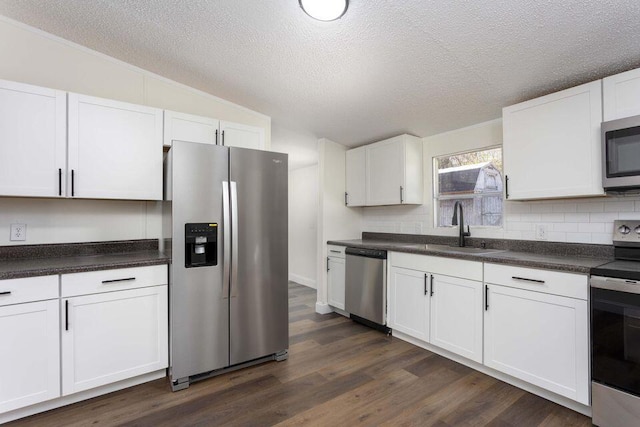 kitchen with white cabinets, dark wood finished floors, dark countertops, stainless steel appliances, and a sink