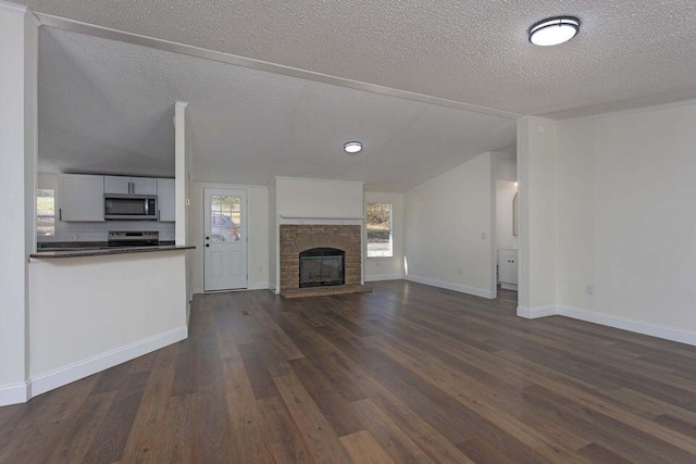 unfurnished living room with baseboards, a glass covered fireplace, dark wood-type flooring, vaulted ceiling, and a textured ceiling