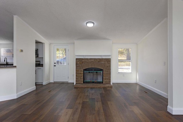 unfurnished living room featuring plenty of natural light, baseboards, dark wood-type flooring, and a stone fireplace