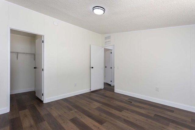 unfurnished bedroom featuring a textured ceiling, a spacious closet, dark wood-type flooring, and a closet