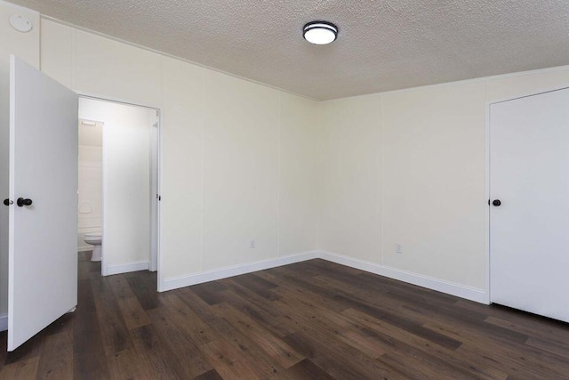 unfurnished bedroom with ensuite bath, a textured ceiling, and dark wood-style flooring