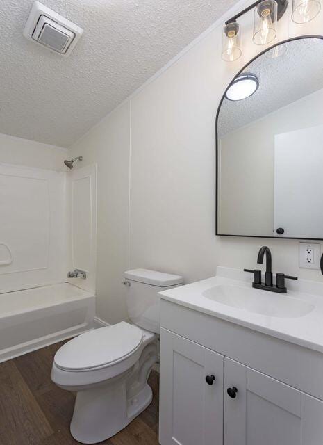 full bath with visible vents, wood finished floors, a textured ceiling, vanity, and washtub / shower combination