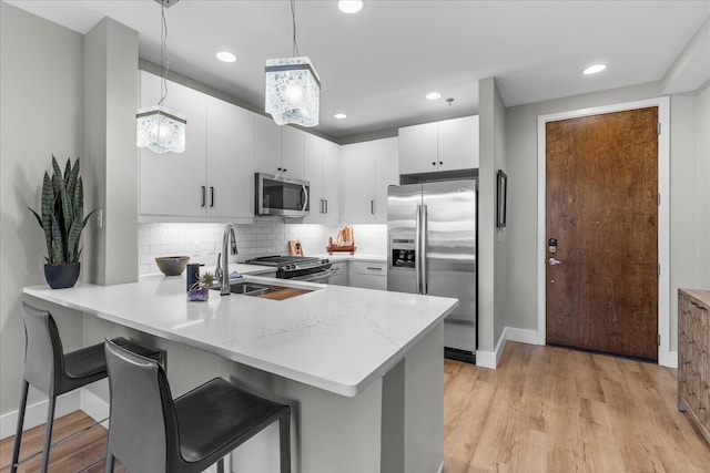 kitchen with stainless steel appliances, a peninsula, a sink, light wood finished floors, and tasteful backsplash