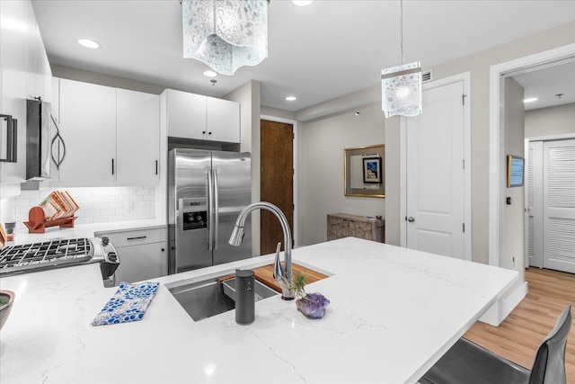 kitchen with light stone counters, stainless steel appliances, light wood-type flooring, backsplash, and pendant lighting