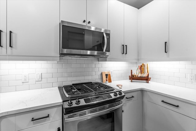 kitchen with tasteful backsplash, appliances with stainless steel finishes, white cabinets, and light stone counters