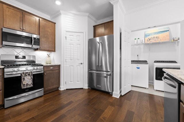 kitchen featuring dark wood-style flooring, washer and dryer, appliances with stainless steel finishes, light stone countertops, and tasteful backsplash