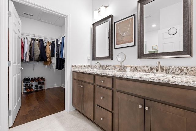 full bath with double vanity, a sink, visible vents, and a walk in closet