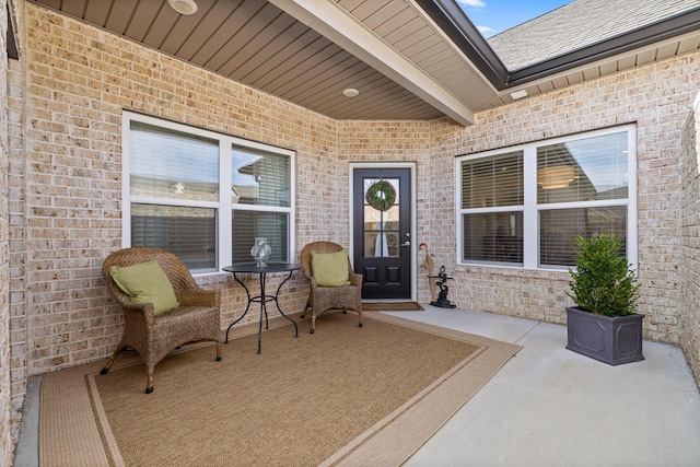 entrance to property with a patio, brick siding, and roof with shingles