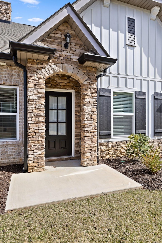 entrance to property with board and batten siding, stone siding, and roof with shingles