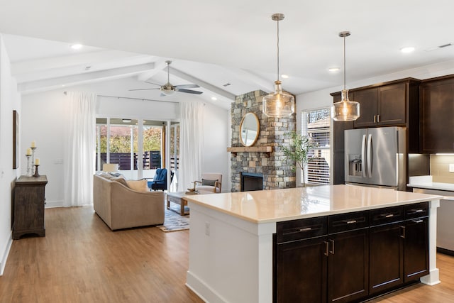 kitchen featuring pendant lighting, vaulted ceiling with beams, stainless steel refrigerator with ice dispenser, light countertops, and open floor plan