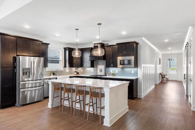 kitchen featuring a kitchen island, appliances with stainless steel finishes, decorative light fixtures, light countertops, and premium range hood