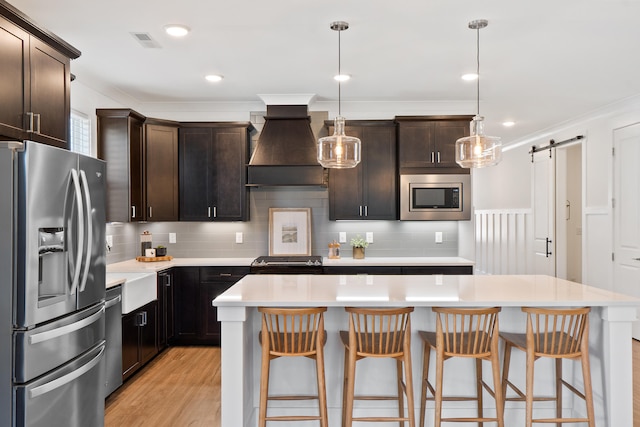 kitchen with a barn door, stainless steel appliances, light countertops, custom exhaust hood, and pendant lighting