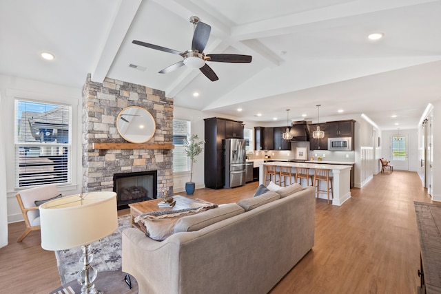 living area with light wood finished floors, baseboards, visible vents, lofted ceiling with beams, and a fireplace