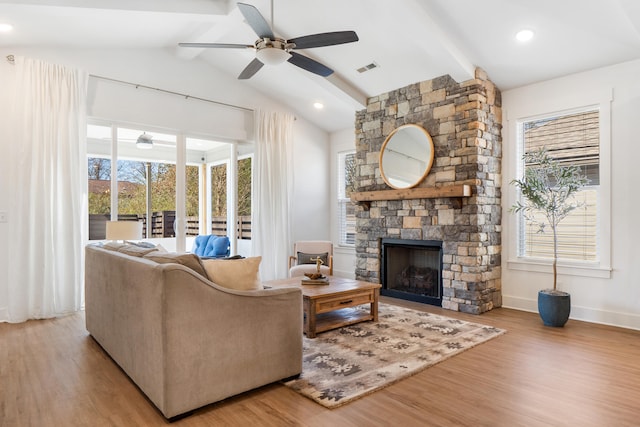 living room with a healthy amount of sunlight, vaulted ceiling with beams, light wood-style flooring, and a stone fireplace