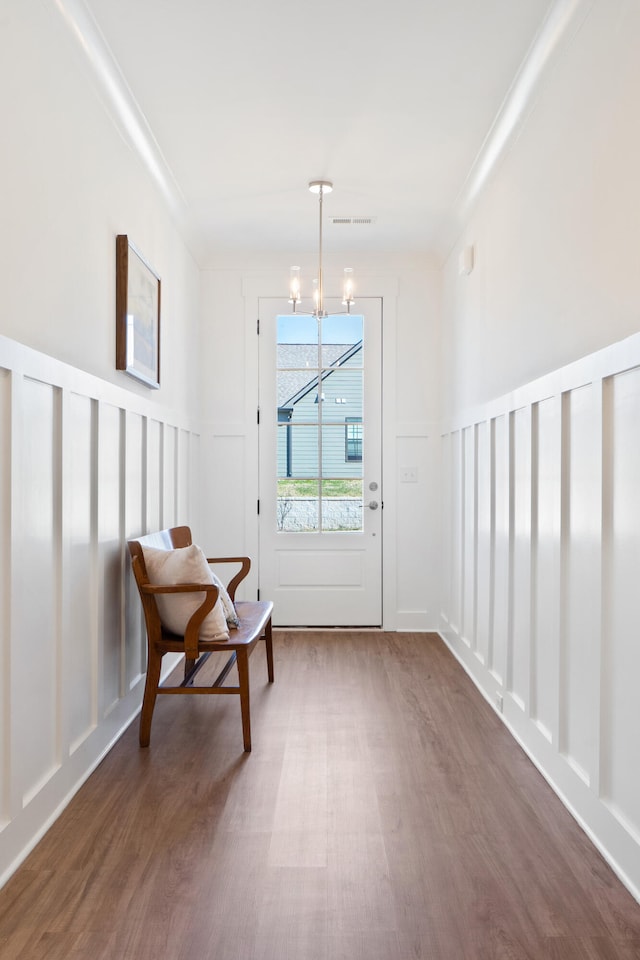 doorway featuring dark wood finished floors, ornamental molding, a decorative wall, and a notable chandelier