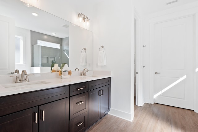 full bathroom with double vanity, a stall shower, a sink, and wood finished floors