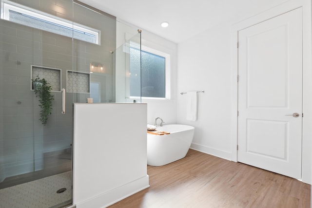 full bathroom with a freestanding bath, baseboards, wood finished floors, and a tile shower