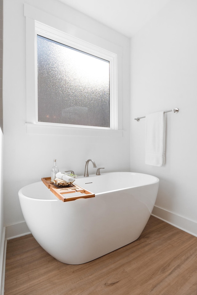 full bath featuring a soaking tub, wood finished floors, and baseboards