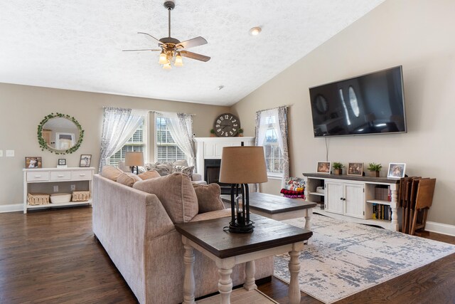 living room with a textured ceiling, dark wood-style flooring, a fireplace, baseboards, and vaulted ceiling