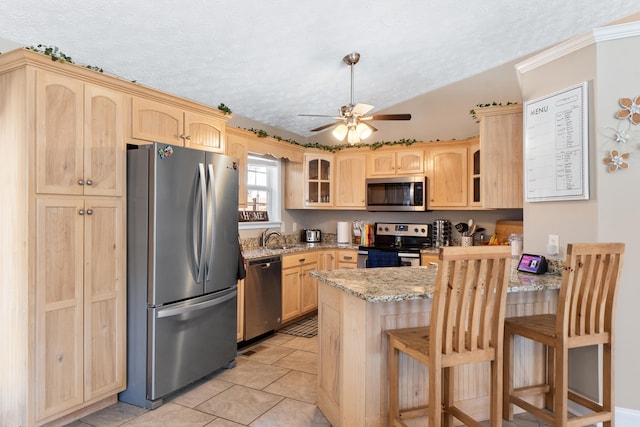 kitchen featuring light stone counters, stainless steel appliances, a peninsula, a breakfast bar, and glass insert cabinets