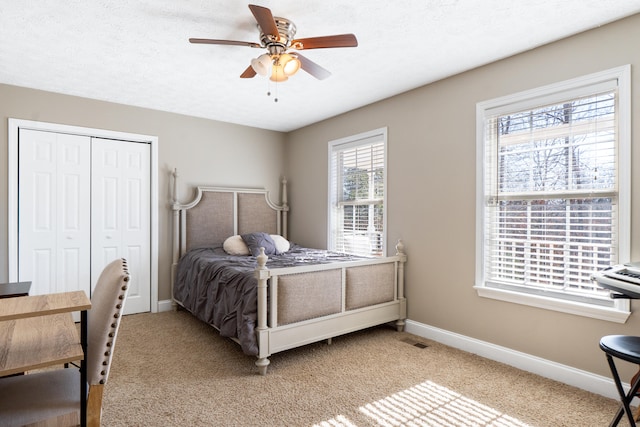bedroom with a textured ceiling, light colored carpet, visible vents, baseboards, and a closet