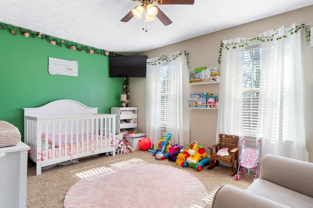 bedroom with a nursery area, multiple windows, a textured ceiling, and light colored carpet