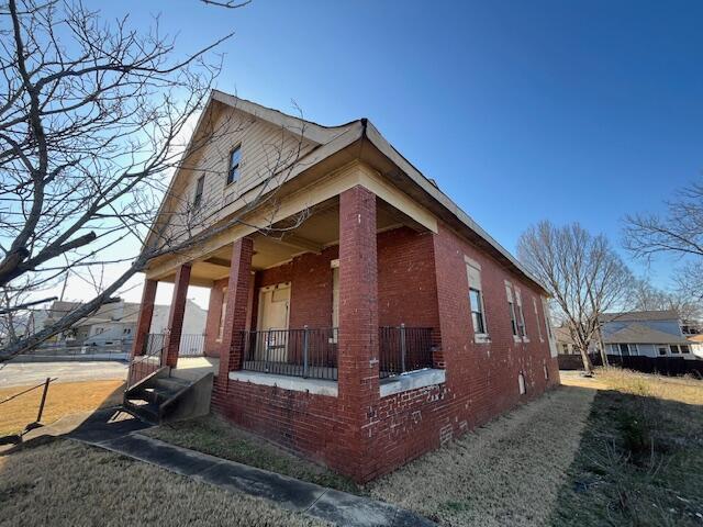 view of home's exterior with a porch, crawl space, and brick siding