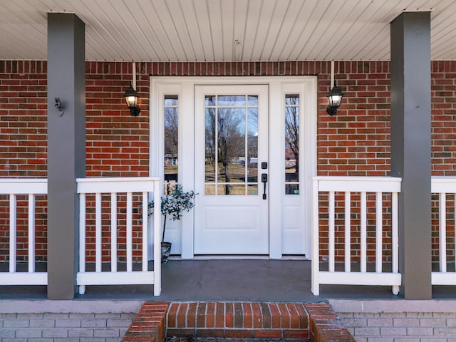 entrance to property with a porch and brick siding