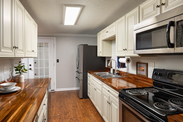 kitchen featuring butcher block counters, dark wood-type flooring, a sink, ornamental molding, and appliances with stainless steel finishes