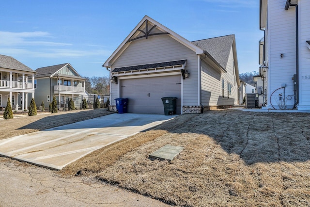 view of side of home with a garage, a shingled roof, cooling unit, and concrete driveway