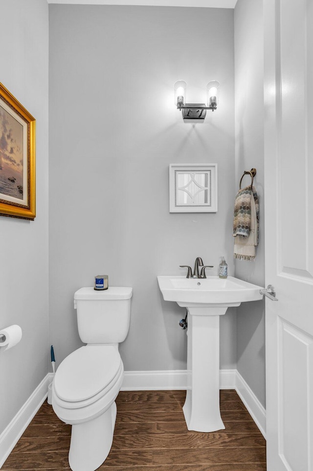 half bath with toilet, baseboards, and wood finished floors